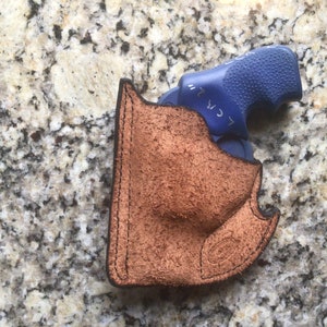 May include: A brown leather holster with a blue handgun inside. The holster is made of textured leather and has black stitching around the edges. The handgun has a blue grip. The image is taken from a top-down perspective.