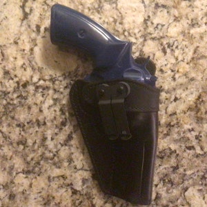 May include: A blue revolver handgun in a black leather holster with a metal clip.