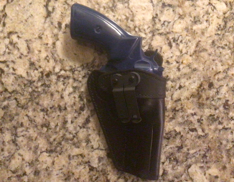 May include: A blue revolver handgun in a black leather holster with a metal clip.
