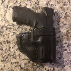 May include: A black leather holster with a black handgun inside. The holster has a belt loop and a snap closure.