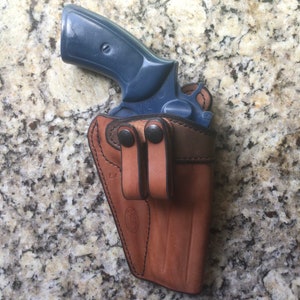 Puede incluir: Un rev&oacute;lver azul en una funda de cuero marr&oacute;n con dos trabillas para el cintur&oacute;n.