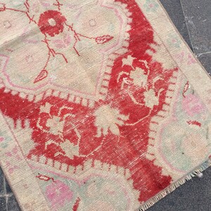 May include: A vintage rug with a cream background and a red floral design. The rug has a fringed edge and is made of woven fabric.