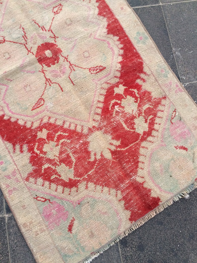 May include: A vintage rug with a cream background and a red floral design. The rug has a fringed edge and is made of woven fabric.