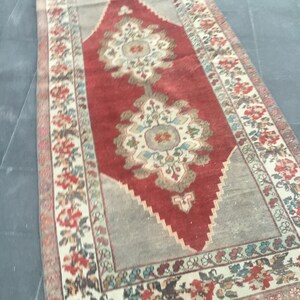 Puede incluir: Una alfombra vintage con un centro rojo y un borde crema. La alfombra tiene un patr&oacute;n floral con detalles intrincados. La alfombra est&aacute; en buen estado y tiene un aspecto desgastado.