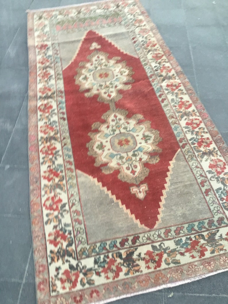 Puede incluir: Una alfombra vintage con un centro rojo y un borde crema. La alfombra tiene un patr&oacute;n floral con detalles intrincados. La alfombra est&aacute; en buen estado y tiene un aspecto desgastado.