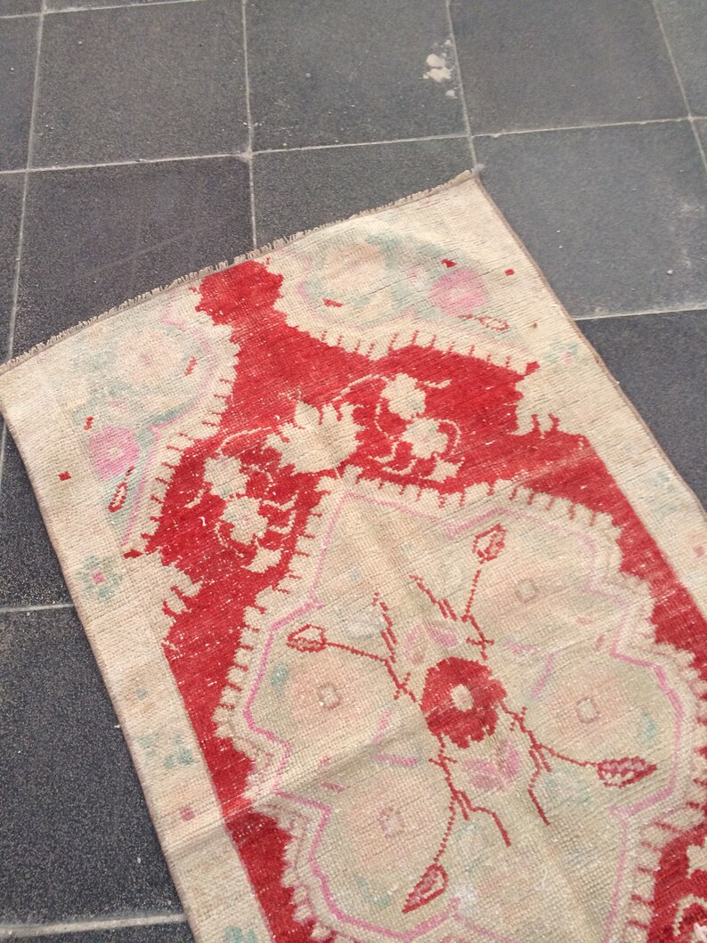 May include: A vintage rug with a cream background and a red floral pattern. The rug has a fringed edge and is made of wool.
