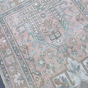 May include: A vintage Turkish rug with a pink and blue geometric pattern. The rug has a faded, distressed look and is made of wool.