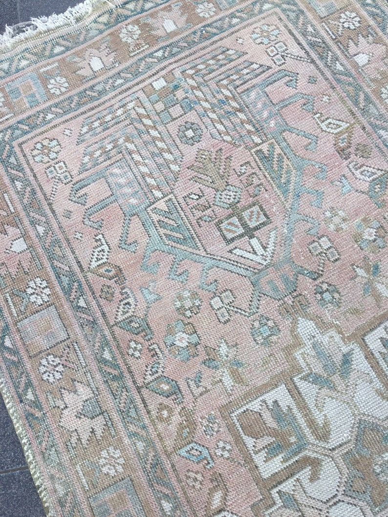 May include: A vintage Turkish rug with a pink and blue geometric pattern. The rug has a faded, distressed look and is made of wool.