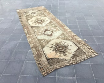 May include: A vintage runner rug with a geometric pattern in shades of brown and cream. The rug has a worn, distressed look and features intricate details.