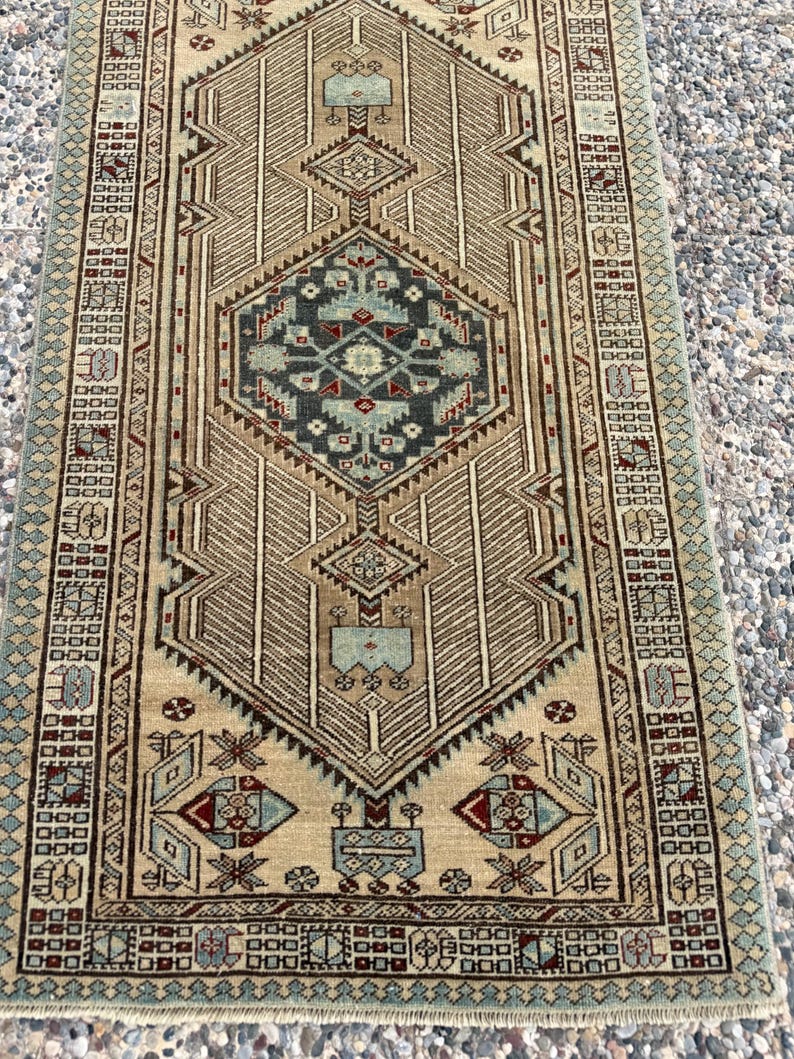 May include: A rectangular area rug featuring a central geometric medallion in shades of teal, dark blue, and deep red against a tan background. The rug is decorated with intricate linear patterns, repeating motifs, and a detailed border design.