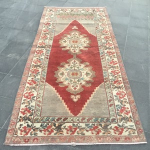 Puede incluir: Una alfombra turca vintage con un centro rojo y un borde crema. La alfombra tiene un patr&oacute;n floral y est&aacute; en buen estado.