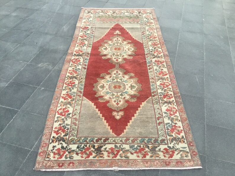 Puede incluir: Una alfombra turca vintage con un centro rojo y un borde crema. La alfombra tiene un patr&oacute;n floral y est&aacute; en buen estado.