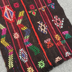 Puede incluir: Una alfombra colorida tejida a mano con fondo negro y intrincados patrones geom&eacute;tricos en tonos rojos, verdes, azules, amarillos y rosas. La alfombra tiene un borde con flecos y est&aacute; hecha de lana.