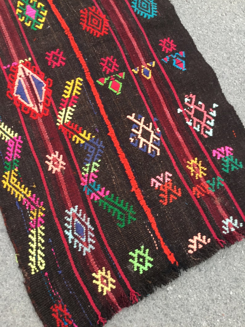 Puede incluir: Una alfombra colorida tejida a mano con fondo negro y intrincados patrones geom&eacute;tricos en tonos rojos, verdes, azules, amarillos y rosas. La alfombra tiene un borde con flecos y est&aacute; hecha de lana.