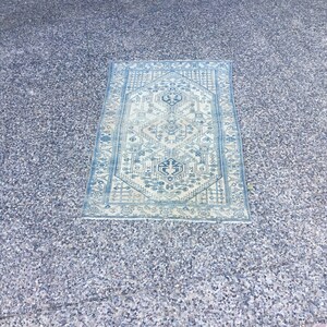 Puede incluir: Una alfombra azul y blanca con un diseño geométrico. La alfombra está colocada sobre una superficie de grava gris.