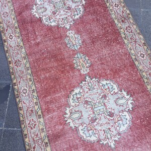 Pode incluir: Um tapete corredor vermelho com um padr&atilde;o floral desbotado e uma borda bege. O tapete tem um aspecto desgastado e &eacute; feito de um material macio e tecido.