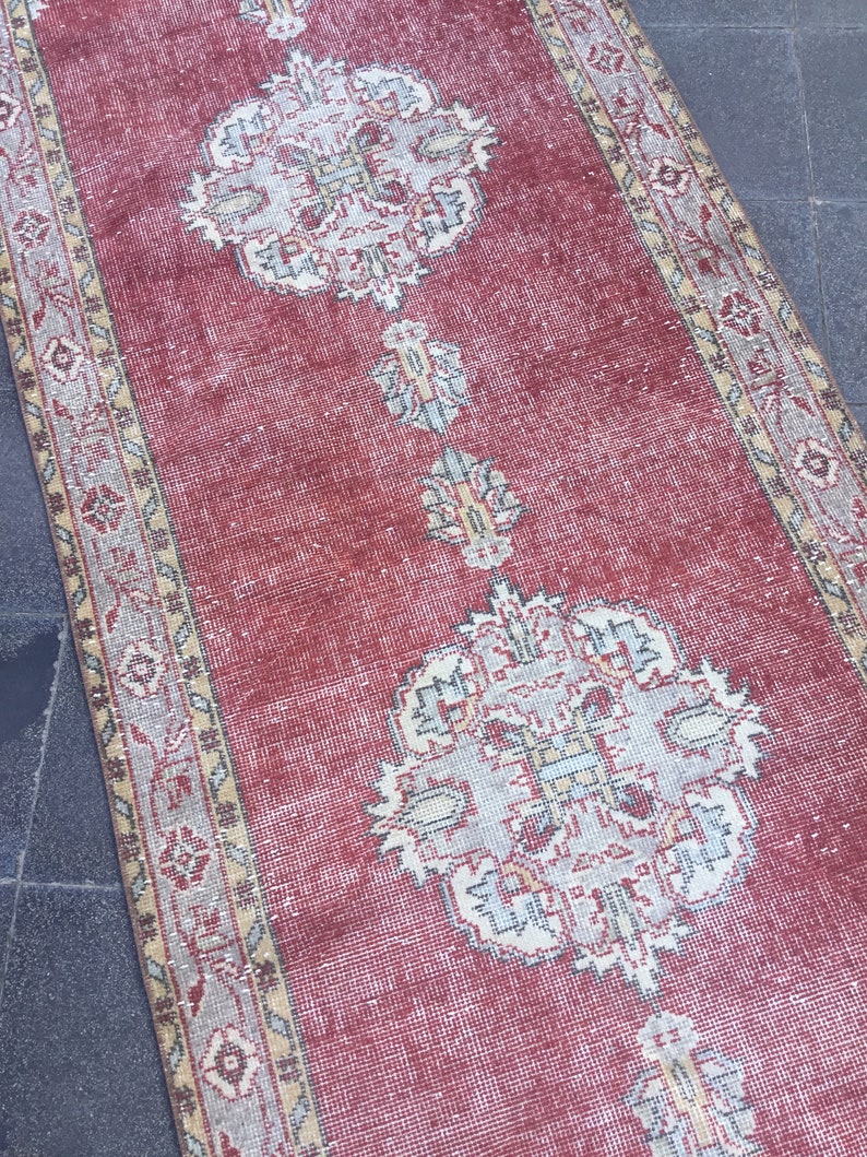 Pode incluir: Um tapete corredor vermelho com um padr&atilde;o floral desbotado e uma borda bege. O tapete tem um aspecto desgastado e &eacute; feito de um material macio e tecido.