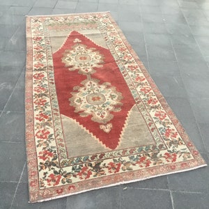 Puede incluir: Una alfombra vintage con un centro rojo y un patr&oacute;n en forma de diamante. La alfombra tiene un borde crema con dise&ntilde;os florales en tonos rojos, verdes y azules.