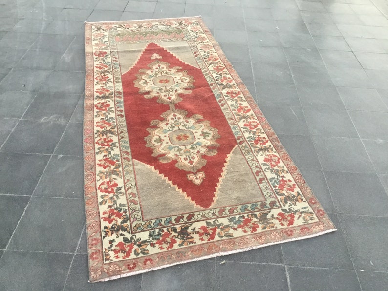Puede incluir: Una alfombra vintage con un centro rojo y un patr&oacute;n en forma de diamante. La alfombra tiene un borde crema con dise&ntilde;os florales en tonos rojos, verdes y azules.
