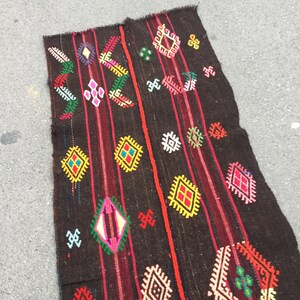 Puede incluir: Una alfombra tejida de color marr&oacute;n oscuro con patrones geom&eacute;tricos coloridos. La alfombra tiene un dise&ntilde;o tradicional con acentos rojos, amarillos, verdes, azules y blancos.