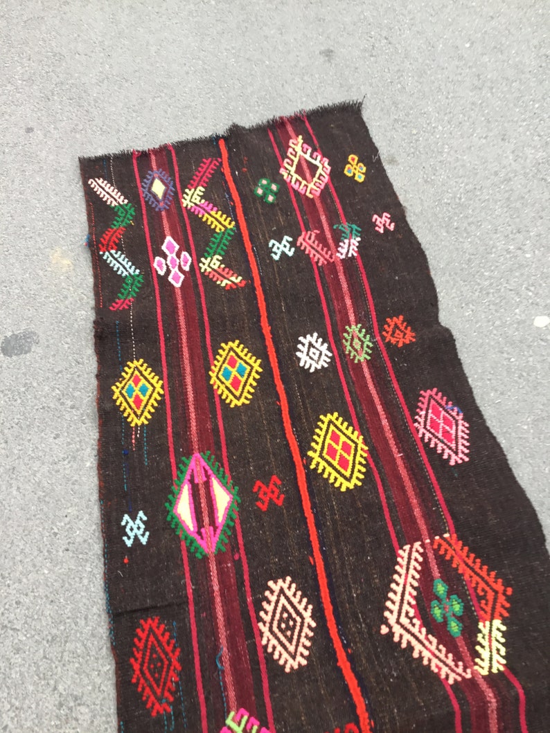 Puede incluir: Una alfombra tejida de color marr&oacute;n oscuro con patrones geom&eacute;tricos coloridos. La alfombra tiene un dise&ntilde;o tradicional con acentos rojos, amarillos, verdes, azules y blancos.