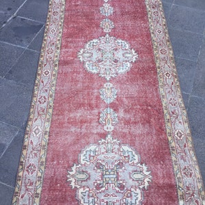 Pode incluir: Um tapete corredor vintage vermelho com um padr&atilde;o floral desbotado. O tapete tem uma borda creme com um design geom&eacute;trico.