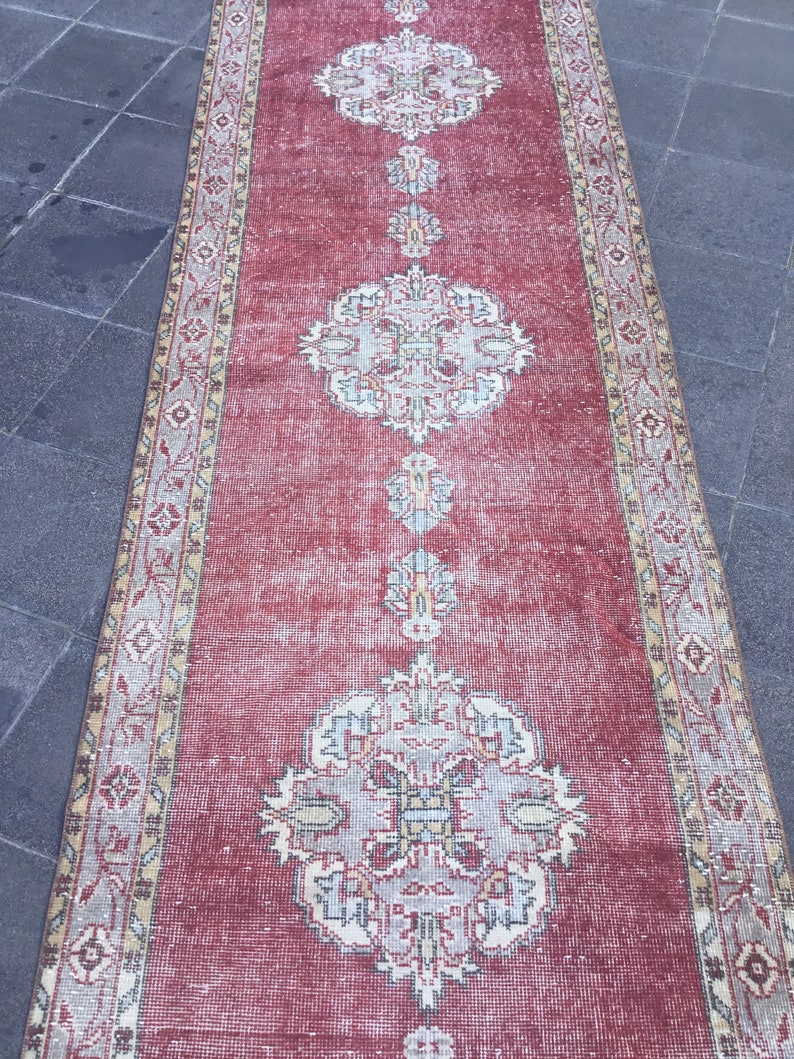 Pode incluir: Um tapete corredor vintage vermelho com um padr&atilde;o floral desbotado. O tapete tem uma borda creme com um design geom&eacute;trico.