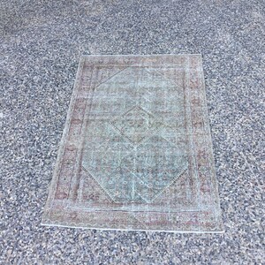 Puede incluir: Una alfombra vintage con un esquema de color verde y azul descolorido. La alfombra tiene un patrón de diamante en el centro y un borde rojo y blanco.