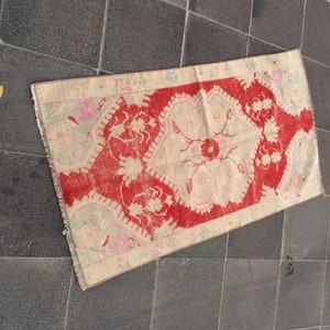 May include: A vintage Turkish rug with a red and cream color scheme. The rug has a floral pattern with a central medallion. The rug is in good condition with some wear and tear.
