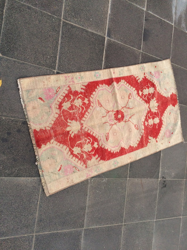 May include: A vintage Turkish rug with a red and cream color scheme. The rug has a floral pattern with a central medallion. The rug is in good condition with some wear and tear.