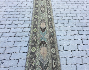 May include: A long, narrow rug with a traditional Persian design. The rug is brown with green, blue, and beige accents. The rug has a fringe on both ends.