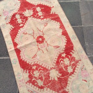 May include: A vintage rug with a red and white floral pattern. The rug has a fringed edge and is made of wool.