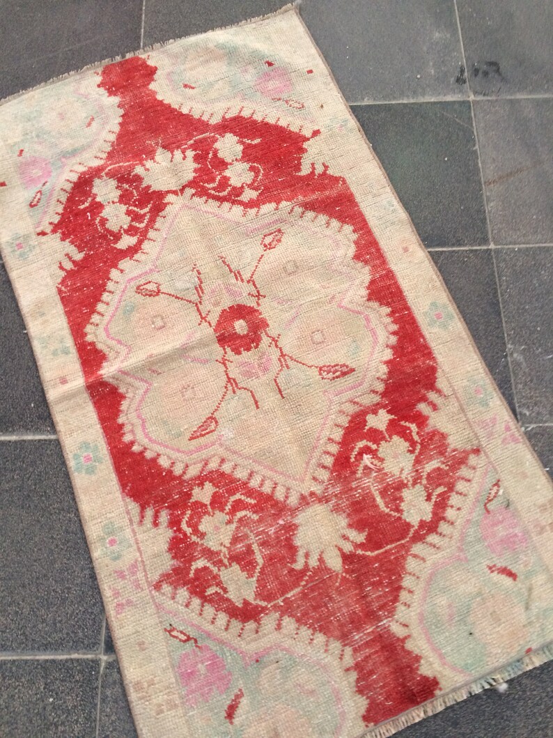 May include: A vintage rug with a red and white floral pattern. The rug has a fringed edge and is made of wool.