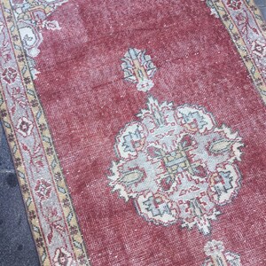 Pode incluir: Um tapete vermelho vintage com um padr&atilde;o floral creme e bege. O tapete tem um aspecto desgastado e &eacute; feito de um material tecido.