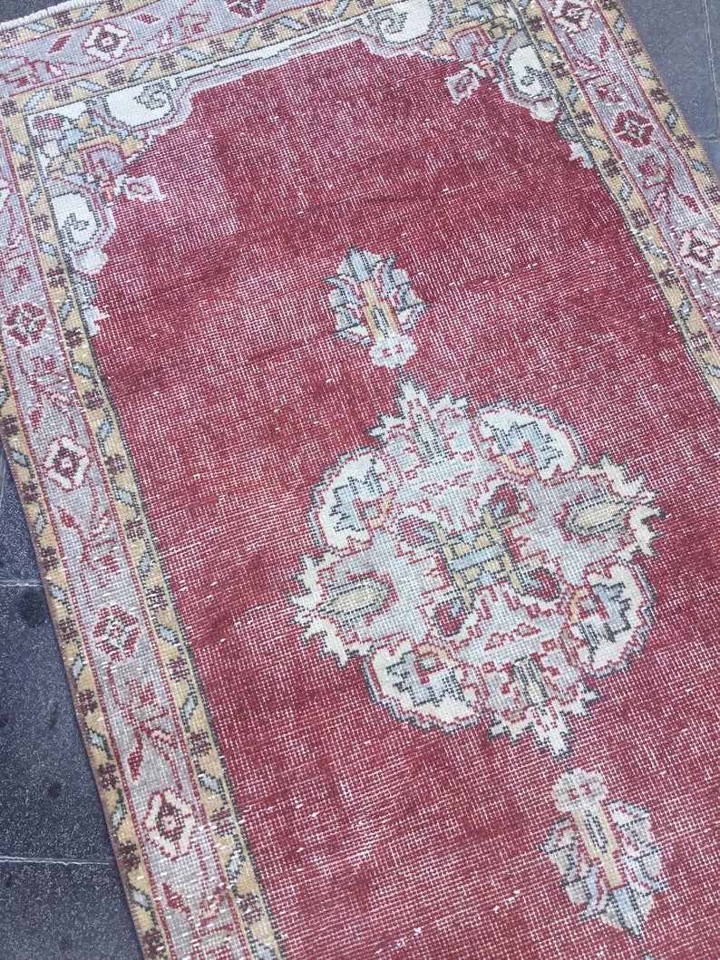 Pode incluir: Um tapete vermelho vintage com um padr&atilde;o floral creme e bege. O tapete tem um aspecto desgastado e &eacute; feito de um material tecido.