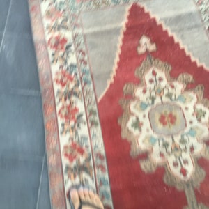 Puede incluir: Un primer plano de una alfombra roja, blanca y azul con un dise&ntilde;o floral. La alfombra tiene un aspecto desgastado y vintage.