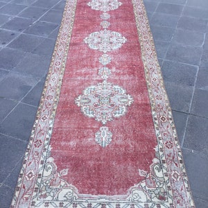 Pode incluir: Um tapete corredor vermelho vintage com uma borda creme e bege e padr&otilde;es florais intrincados. O tapete tem um visual desgastado e &eacute; perfeito para adicionar um toque de estilo bo&eacute;mio a qualquer c&ocirc;modo.