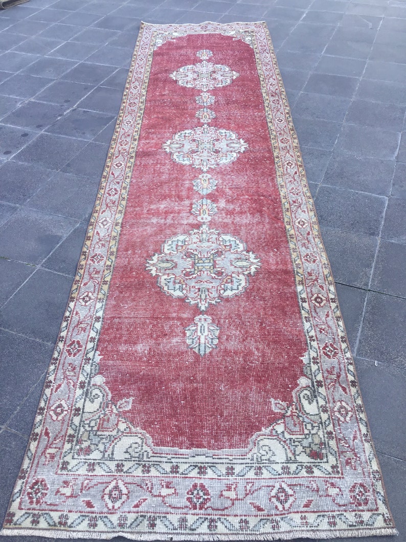 Pode incluir: Um tapete corredor vermelho vintage com uma borda creme e bege e padr&otilde;es florais intrincados. O tapete tem um visual desgastado e &eacute; perfeito para adicionar um toque de estilo bo&eacute;mio a qualquer c&ocirc;modo.