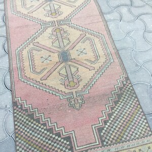 Peut inclure: Tapis rectangulaire de style vintage, aux tons rose et beige. Le tapis pr&eacute;sente des motifs g&eacute;om&eacute;triques dans les tons rose, beige, gris et jaune. Le design comprend des motifs en forme de losanges et de croix, cr&eacute;ant une esth&eacute;tique traditionnelle.