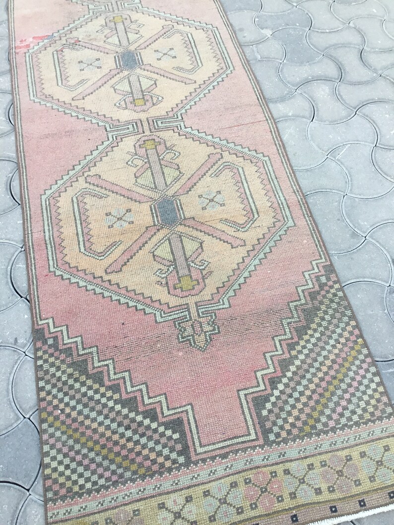 Peut inclure: Tapis rectangulaire de style vintage, aux tons rose et beige. Le tapis pr&eacute;sente des motifs g&eacute;om&eacute;triques dans les tons rose, beige, gris et jaune. Le design comprend des motifs en forme de losanges et de croix, cr&eacute;ant une esth&eacute;tique traditionnelle.