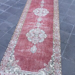 Pode incluir: Um tapete corredor vermelho vintage com um padr&atilde;o floral desbotado e uma borda branca. O tapete tem um visual desgastado e &eacute; perfeito para adicionar um toque de estilo bo&ecirc;mio &agrave; sua casa.