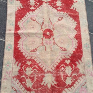 May include: A vintage rug with a floral pattern in shades of red, pink, and white. The rug has a distressed look and is made of a soft, woven material.