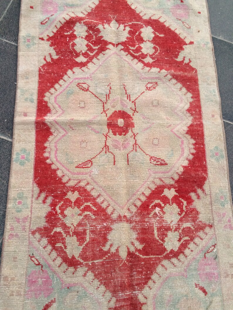 May include: A vintage rug with a floral pattern in shades of red, pink, and white. The rug has a distressed look and is made of a soft, woven material.