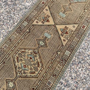 May include: A long runner rug featuring a tan background with intricate geometric patterns in shades of light blue, deep red, and dark brown. The design includes repeating hexagonal medallions and detailed borders with small square motifs.