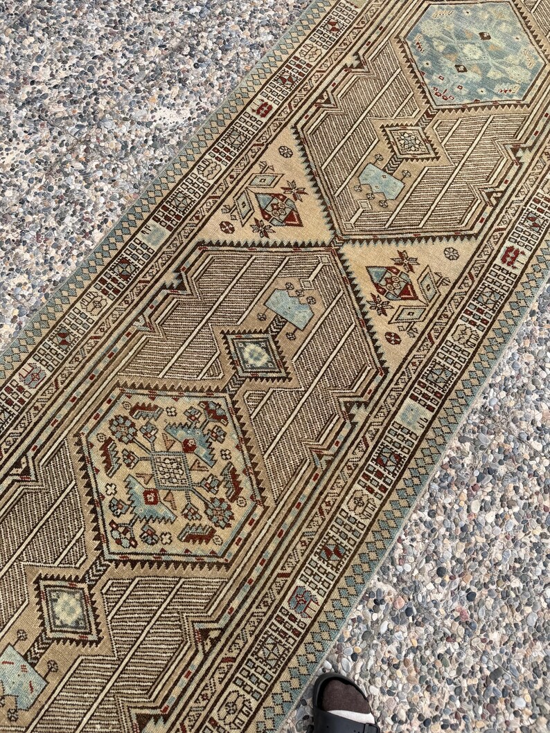 May include: A long runner rug featuring a tan background with intricate geometric patterns in shades of light blue, deep red, and dark brown. The design includes repeating hexagonal medallions and detailed borders with small square motifs.