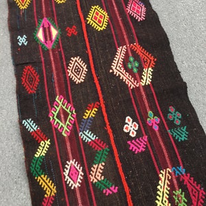 Puede incluir: Una alfombra larga de color marr&oacute;n oscuro con un patr&oacute;n geom&eacute;trico colorido. La alfombra presenta una variedad de formas, incluyendo diamantes, cuadrados y tri&aacute;ngulos, en tonos de rojo, verde, amarillo, azul y rosa.