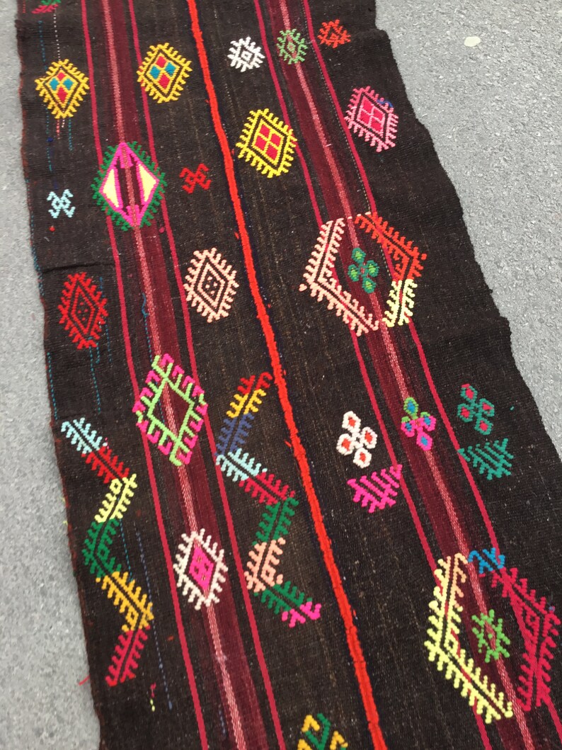 Puede incluir: Una alfombra larga de color marr&oacute;n oscuro con un patr&oacute;n geom&eacute;trico colorido. La alfombra presenta una variedad de formas, incluyendo diamantes, cuadrados y tri&aacute;ngulos, en tonos de rojo, verde, amarillo, azul y rosa.