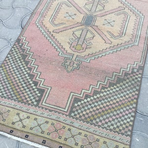 Peut inclure: Un tapis rectangulaire vintage avec un champ central rose et des motifs g&eacute;om&eacute;triques complexes en beige, gris et vert. Le tapis pr&eacute;sente un motif de m&eacute;daillon central et une bordure &agrave; motifs. Les dimensions du tapis ne sont pas visibles.
