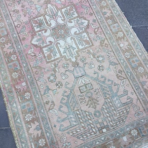 May include: A vintage Turkish runner rug with a pink and green geometric pattern. The rug has a faded, distressed look and features a central medallion design.
