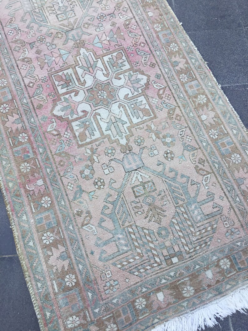 May include: A vintage Turkish runner rug with a pink and green geometric pattern. The rug has a faded, distressed look and features a central medallion design.